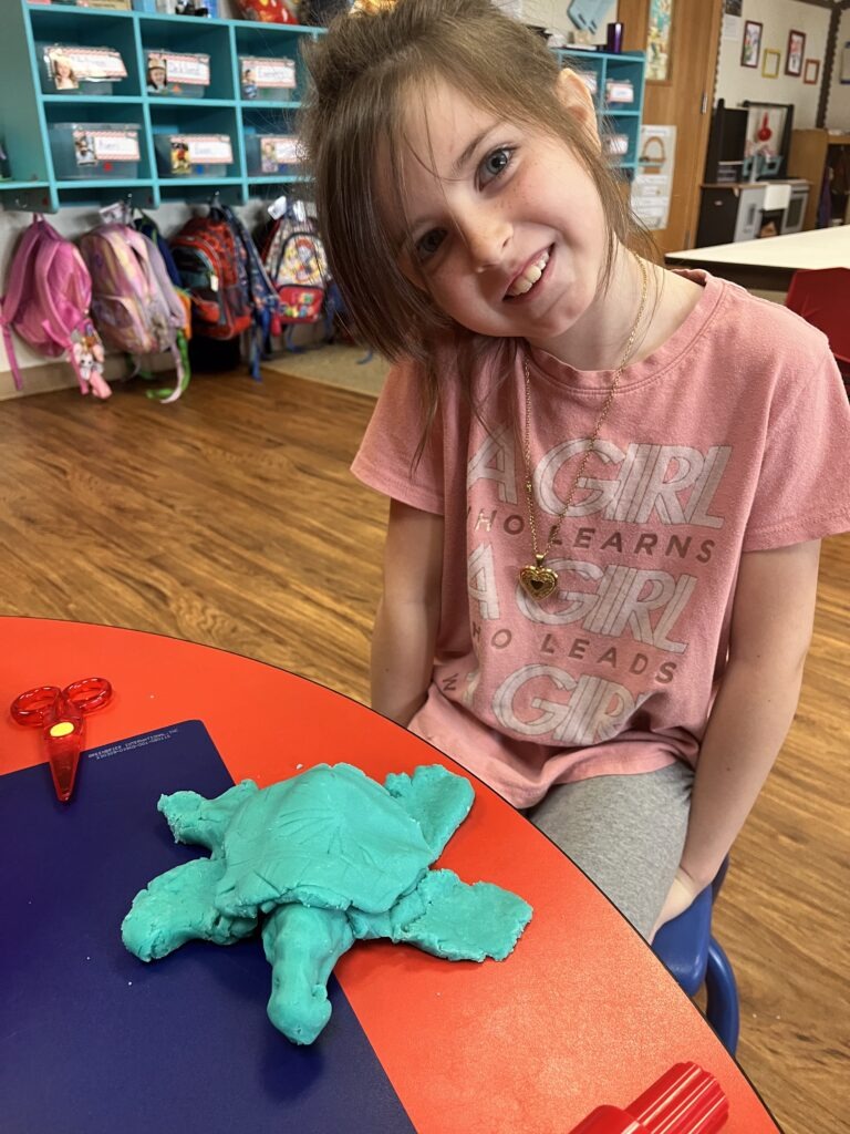 Girl proudly showing her clay turtle sculpture